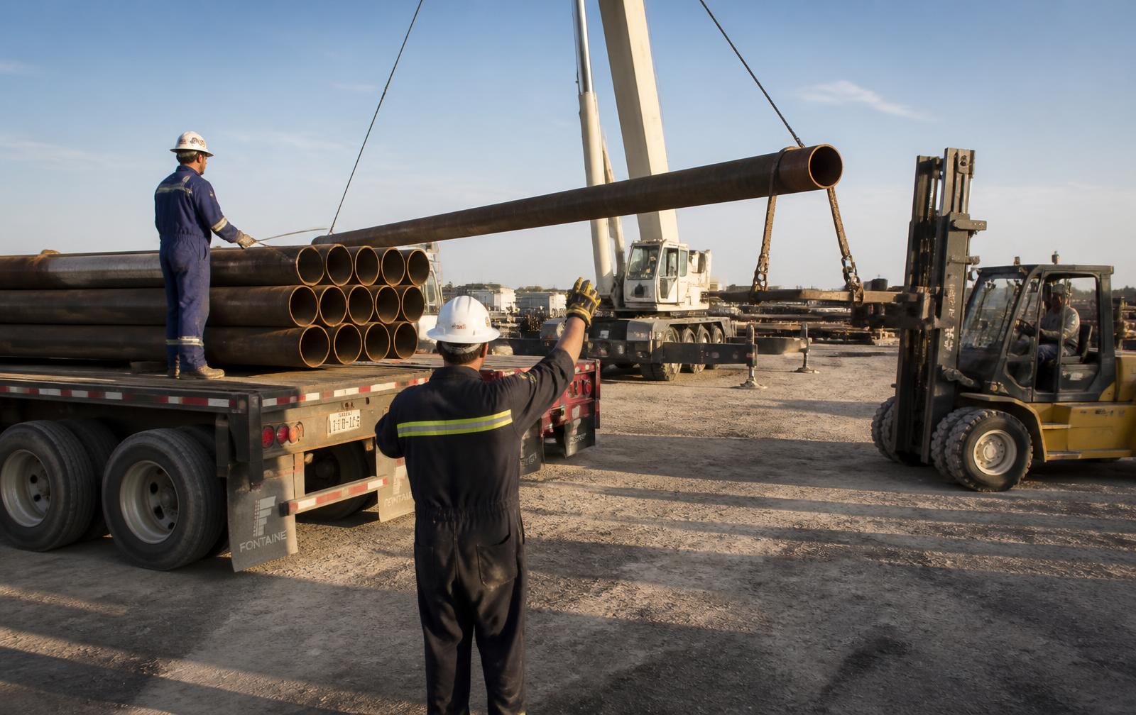 Crane and forklift loading production pipe onto a flatbed trailer